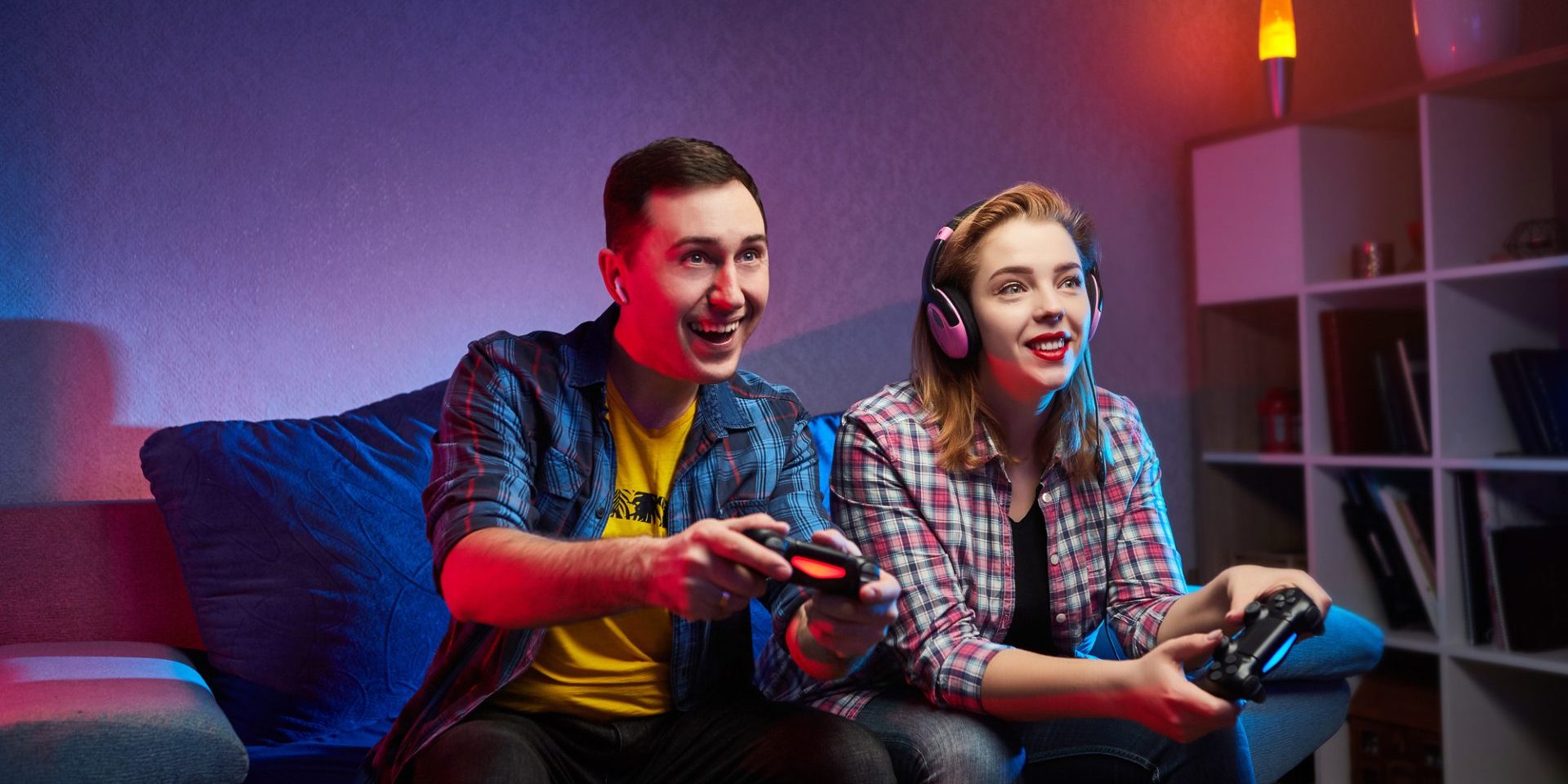 Portrait of crazy playful couple, Gamers enjoying Playing Video Games indoors sitting on the sofa, holding Console Gamepad in hands. Resting At Home, have a great Weekend