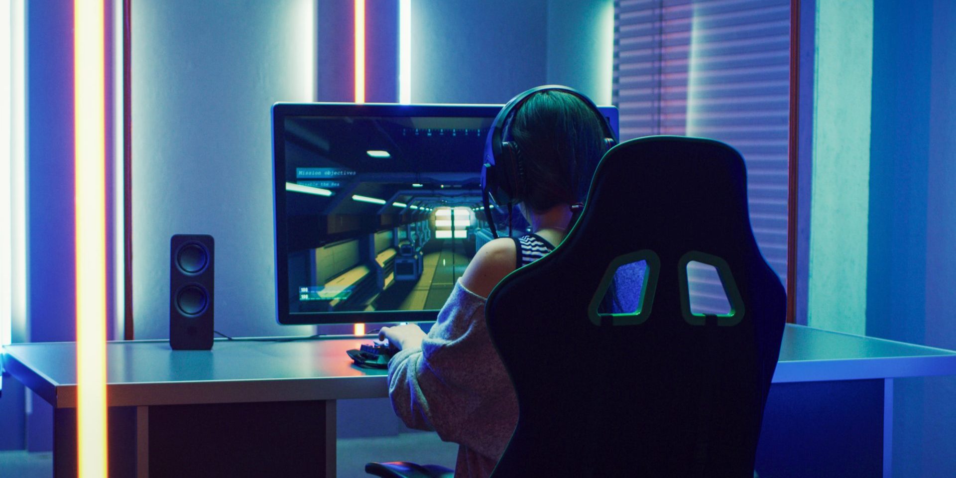 Beautiful Professional Gamer Girl Playing in First-Person Shooter Online Video Game on Her Personal Computer. Casual Cute Geek Girl Wearing Headset. Dark Room Suddenly Lit by Neon Lights in Retro Arcade Style.