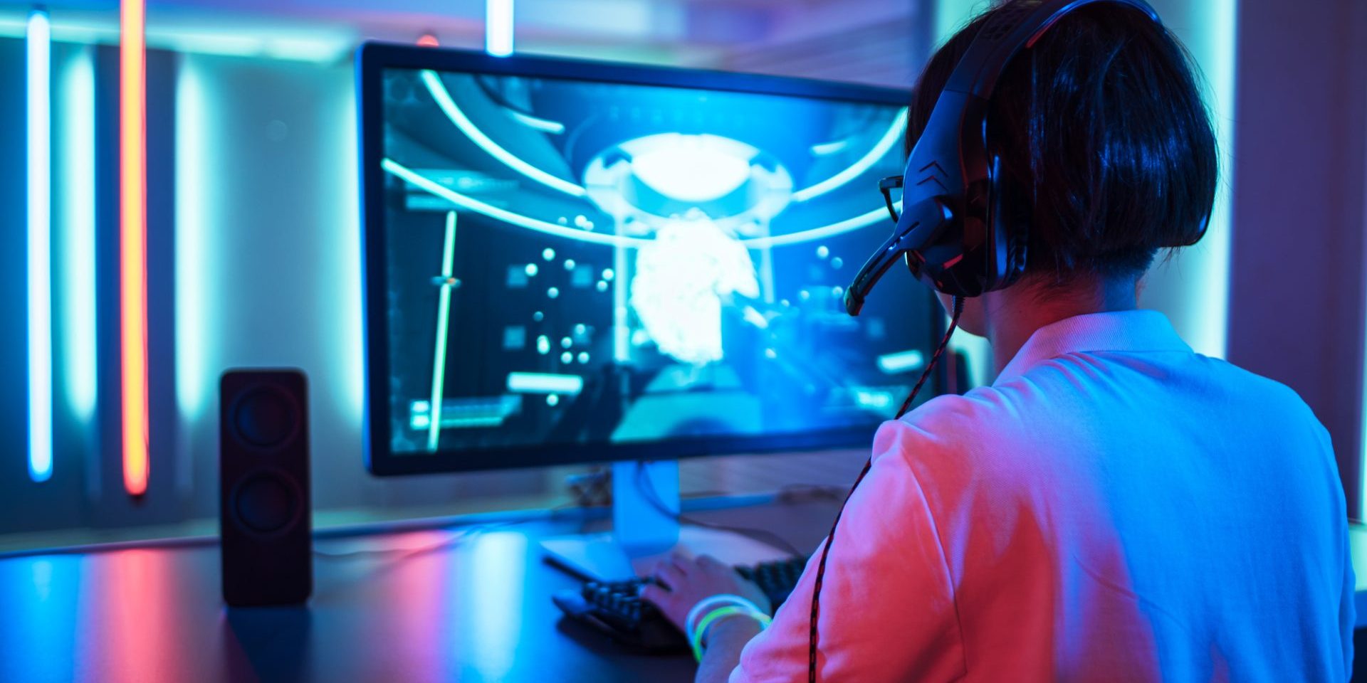 Back View of Professional Gamer Playing in First-Person Shooter Online Video Game on His Personal Computer. Room Lit by Neon Lights in Retro Arcade Style. Cyber Sport Championship.