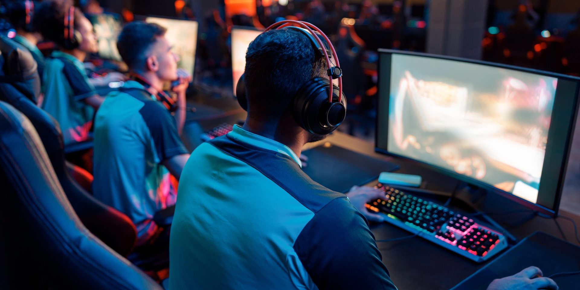 Rear view of professional cybersport gamer playing video games and wearing headphones in dark interior of cybersport club