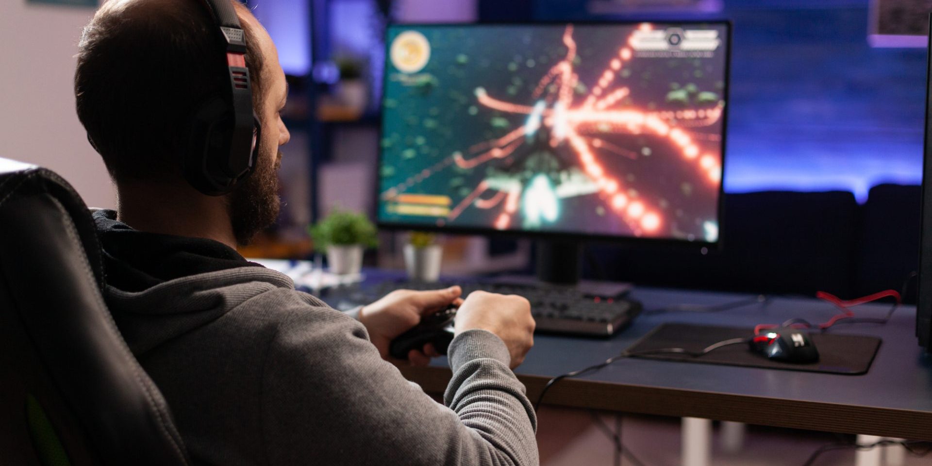 Person playing video games with controller on computer. Player using joystick and wearing headphones to play online game on monitor. Modern man using gaming equipment to have fun.