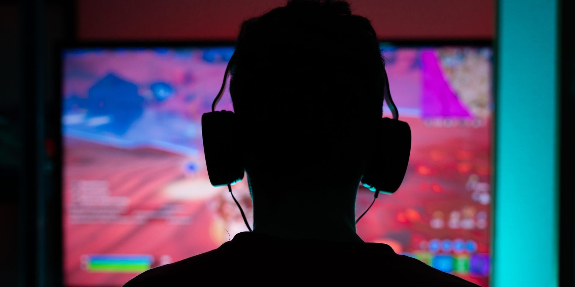 Young guy gamer in headphones plays on the console close-up rear view.