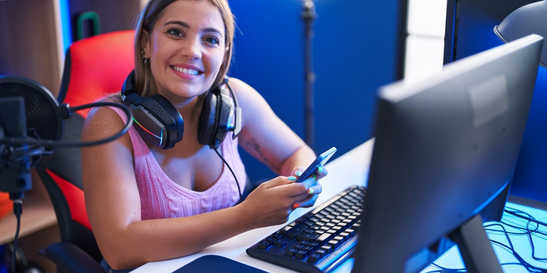 Young beautiful hispanic woman streamer using computer and smartphone at gaming room