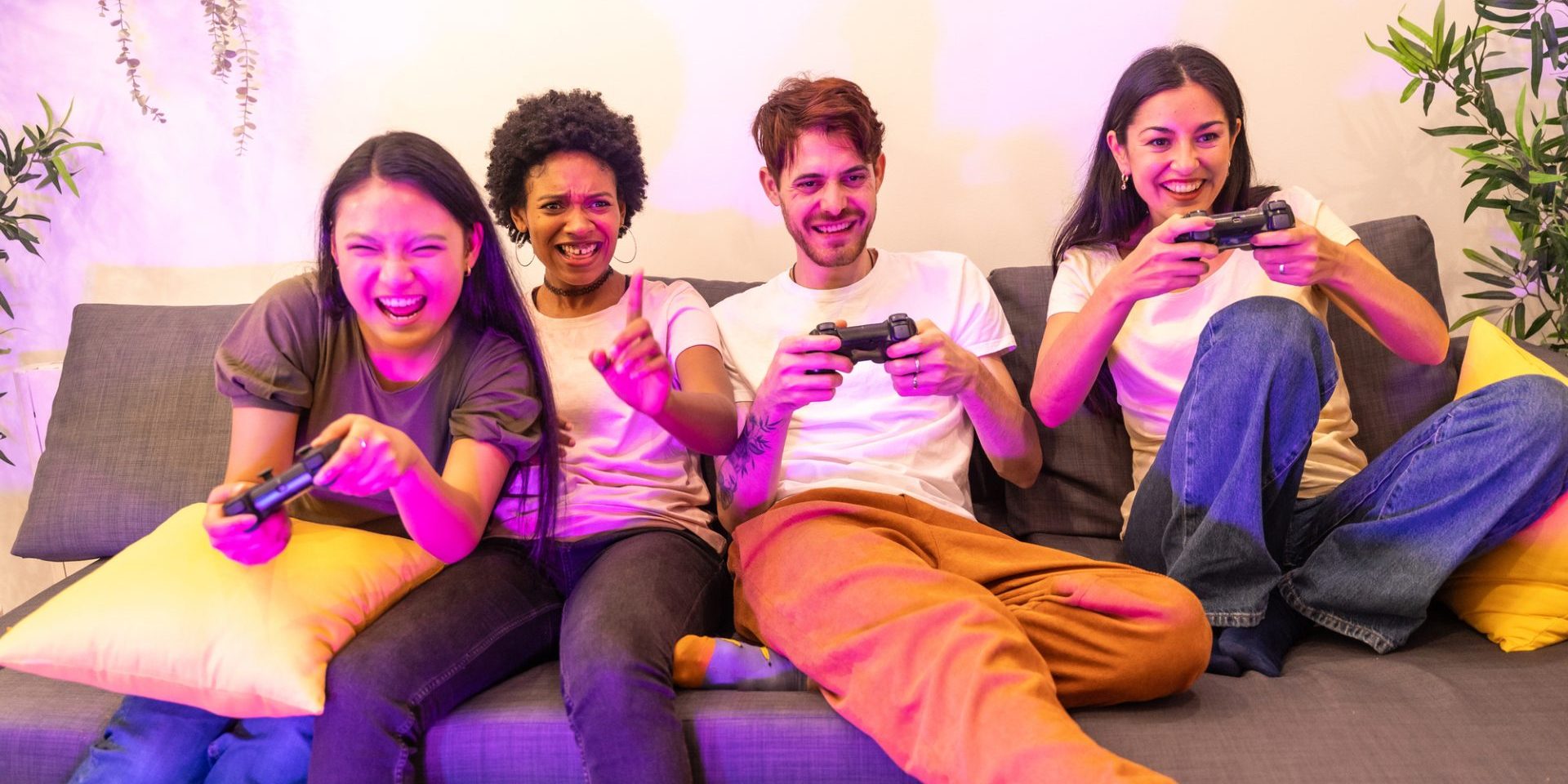 Multi-ethnic friends having fun playing console together sitting on a couch at home